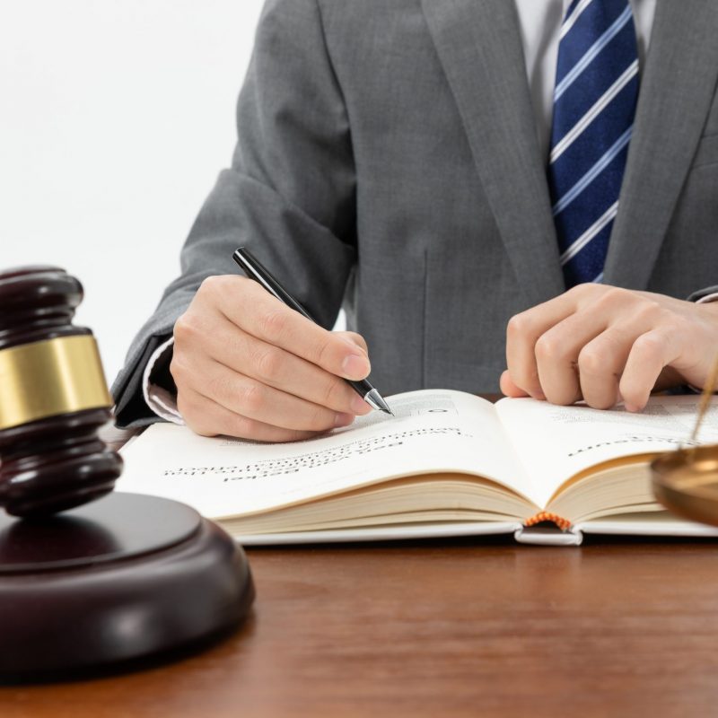 closeup-shot-of-person-writing-in-book-with-gavel-on-the-table